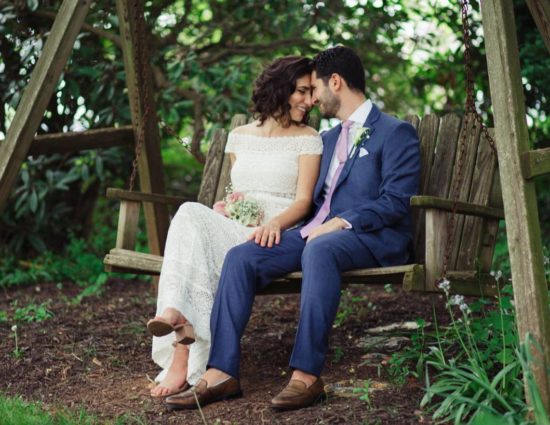 Bride in white dress and groom in purple suit sitting on wooden swing