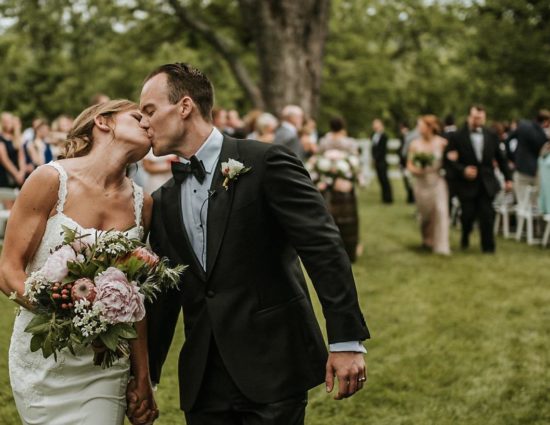 Bride with white dress and groom with black suit walking down the aisle together kissing and holding hands