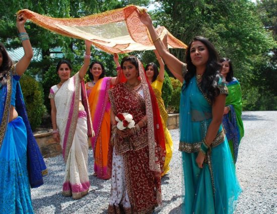 Women dressed in colorful Indian sarees with bride in the middle and scarf held over her head