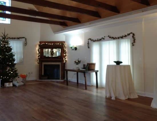 Large room with hardwood flooring, fireplace in the center, and Christmas tree with gifts