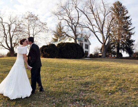 Bride in white dress and groom in black suit standing in grass on front lawn