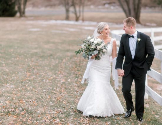 Bride in white dress and groom in black suit standing by white fence