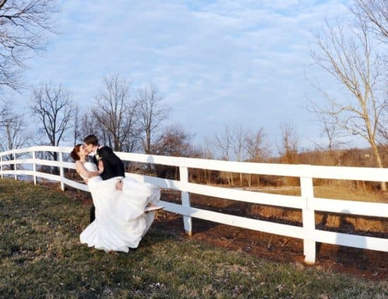 Bride in white dress and groom in black suit standing by white fence