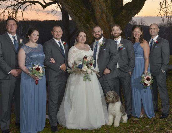 Wedding party with bridesmaids in pale blue dresses, bride in white, and groom and groomsmen in gray suits, and a white and gray dog