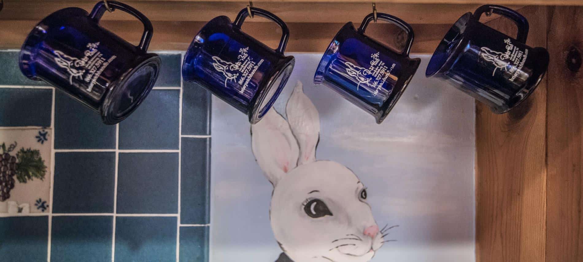 Dark blue mugs with Briar Patch logo hang on metal hooks in front of a white bunny face