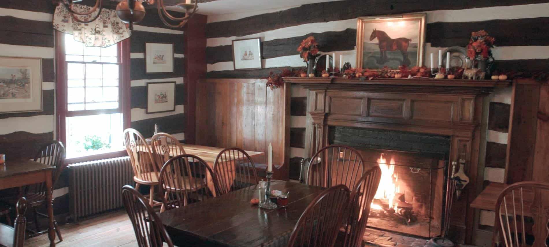 Dining area of restaurant with wooden tables and chairs next to large fireplace with dark wood mantel