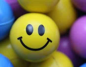 A yellow ball with a black smiley face surrounded by other blue, yellow, and purple balls