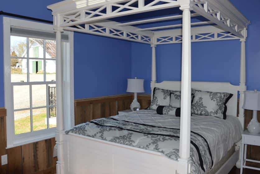 Bedroom with white wooden four-post canopy bed, white and black bedding, wood wainscoating, and blue walls