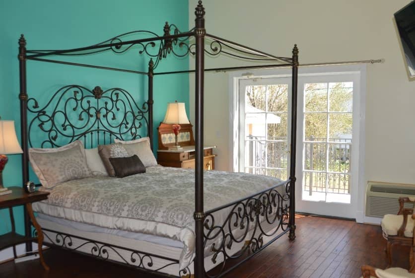 Bedroom with rod iron four-post canopy bed with light tan bedding, hardwood flooring, and a dark turquoise accent wall