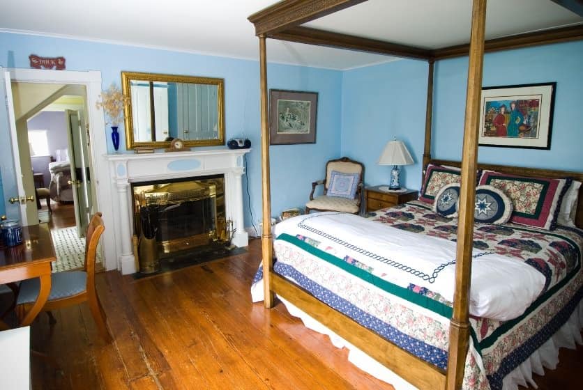 Bedroom with dark wooden furniture and four-post canopy bed, navy, burgundy and white quilt, hardwood floors, fireplace, and blue walls