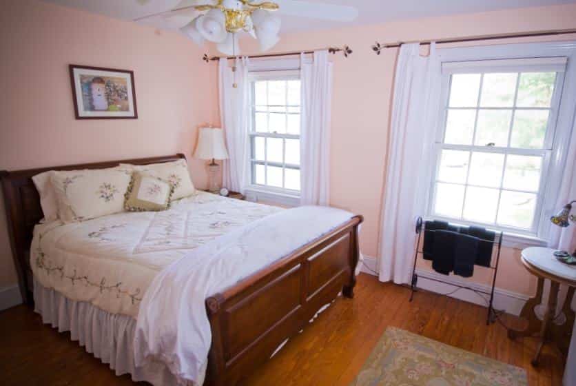 Bedroom with dark wooden sleigh bed, white and cream bedding, hardwood floors, and light pink walls