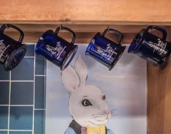 Dark blue mugs with Briar Patch logo hang on metal hooks in front of a white bunny face