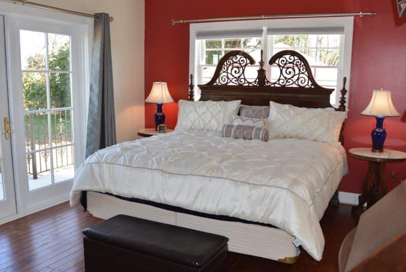 Bedroom with dark wooden ornate headboard, white bedding, hardwood floors, and dark red accent wall