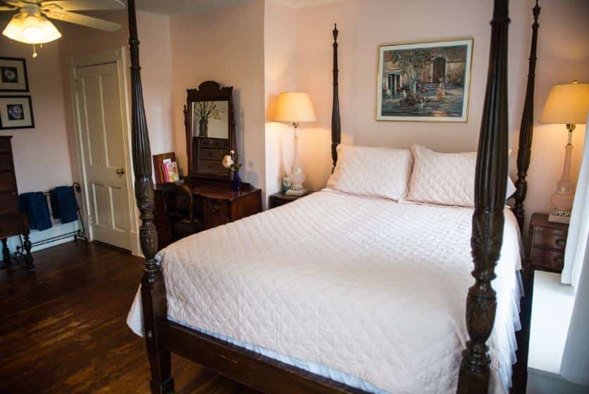 Bedroom with dark wooden furniture, four-post bed, light pink bedding, hardwood floors, and light pink walls