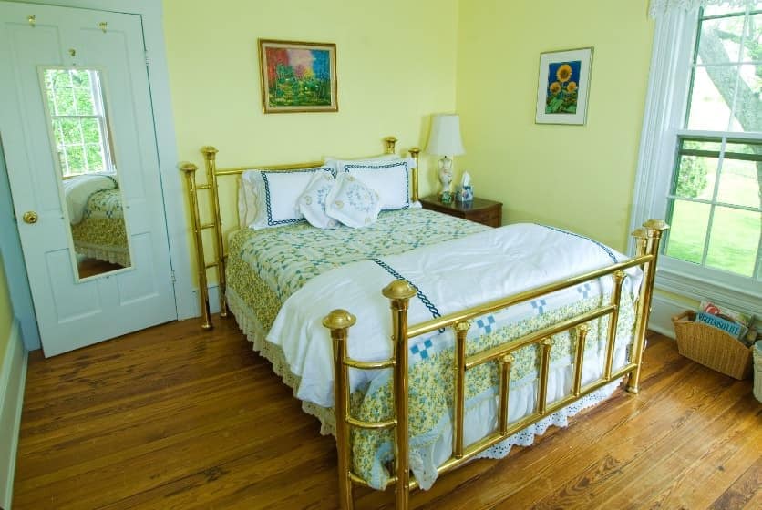 Bedroom with golden brass headboard and footboard, green, blue, and yellow floral quilt, hardwood floors, and yellow walls