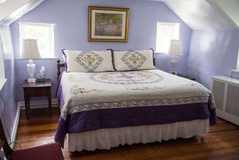 Bedroom with dark wood furniture, dark purple and white bedding, hardwood floors, and light purple walls