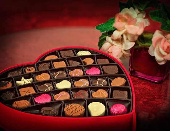 Large red valentine box filled with assorted chocolates next to pink vae with white and pink flowers