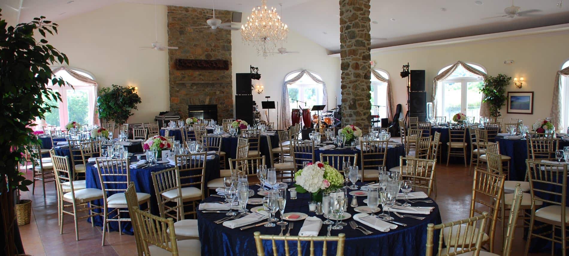 Large room set up with many tables and chairs decorated for an event including a stage with instruments in the corner
