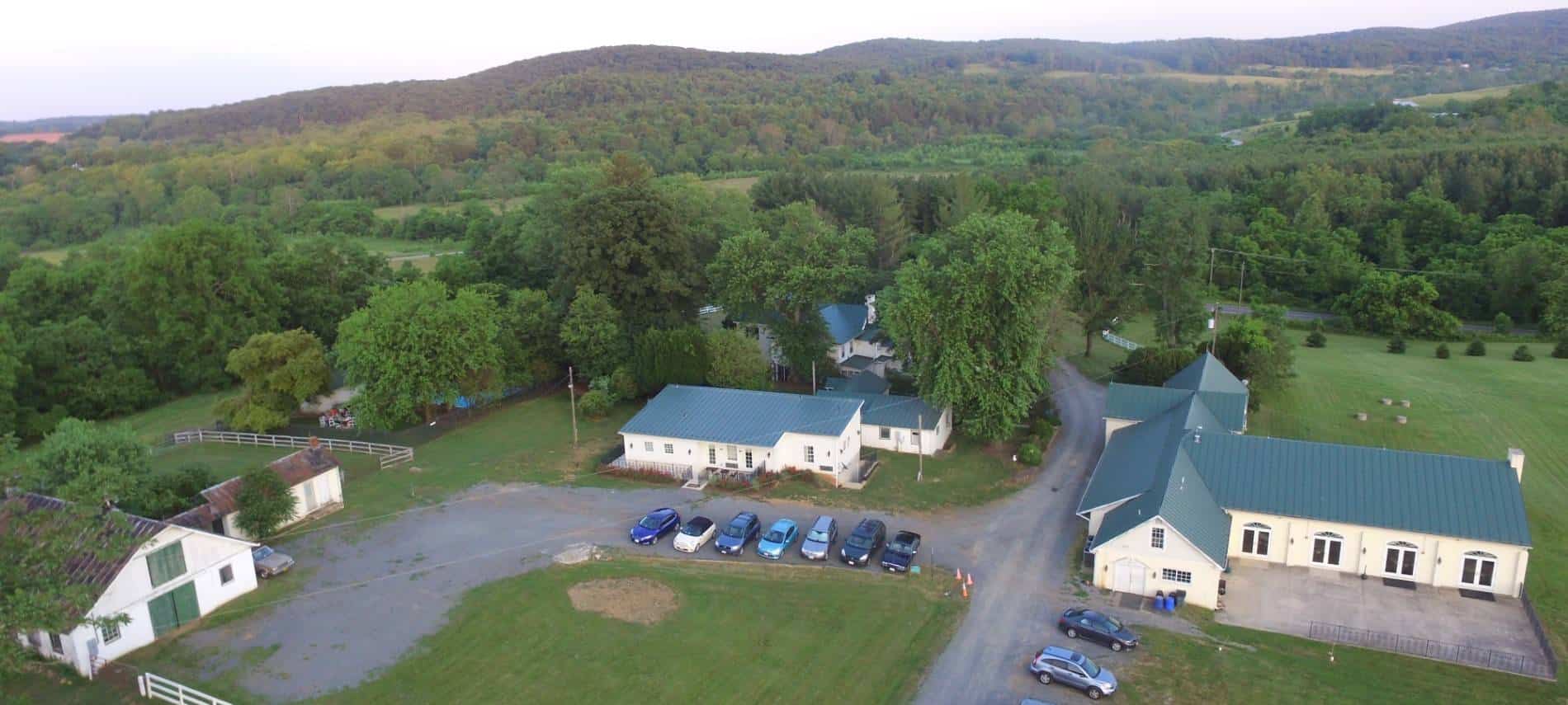 Aerial view of the property surrounded by large trees and green fields