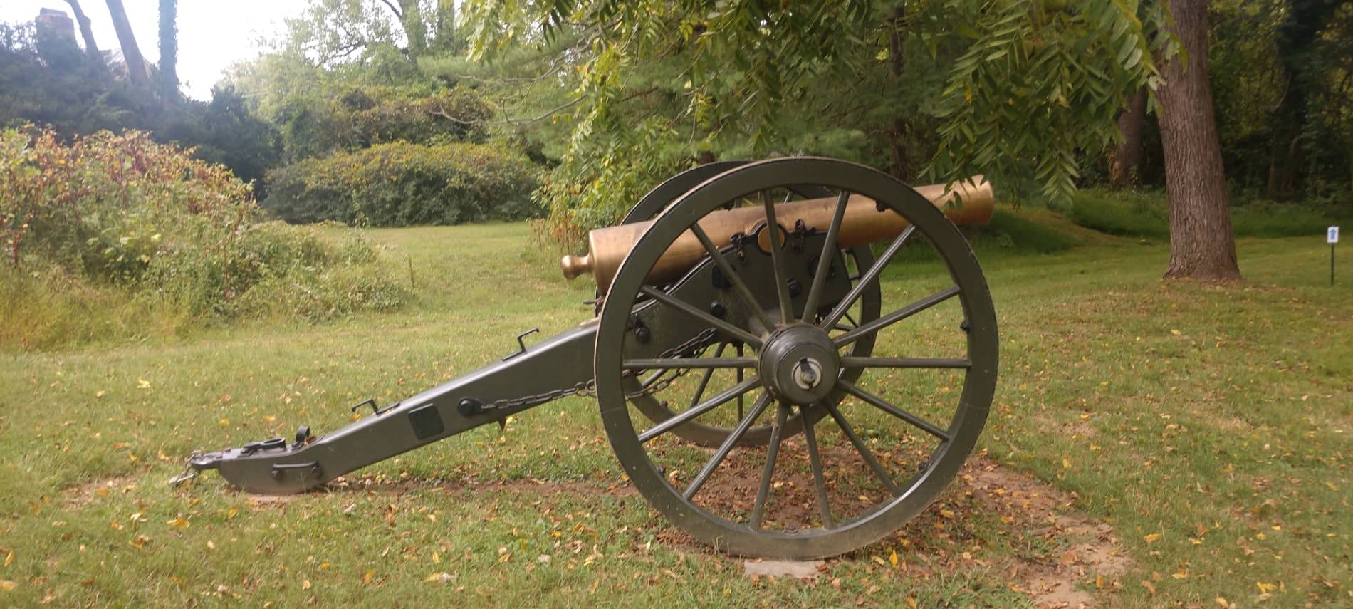 Old military cannon sitting on green grass with green trees in background