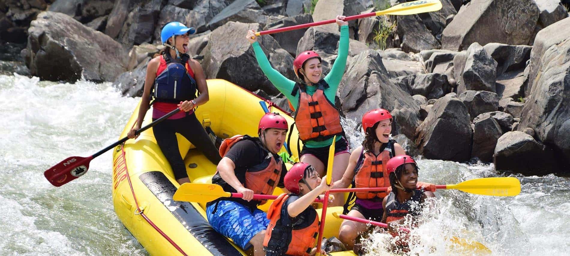 People with lifevests and oars sitting in yellow raft whitewater rafting