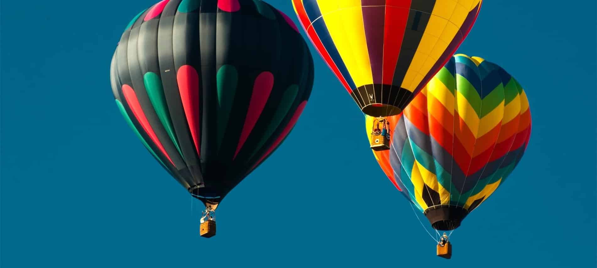 Three brightly colored hot air balloons high in the blue sky