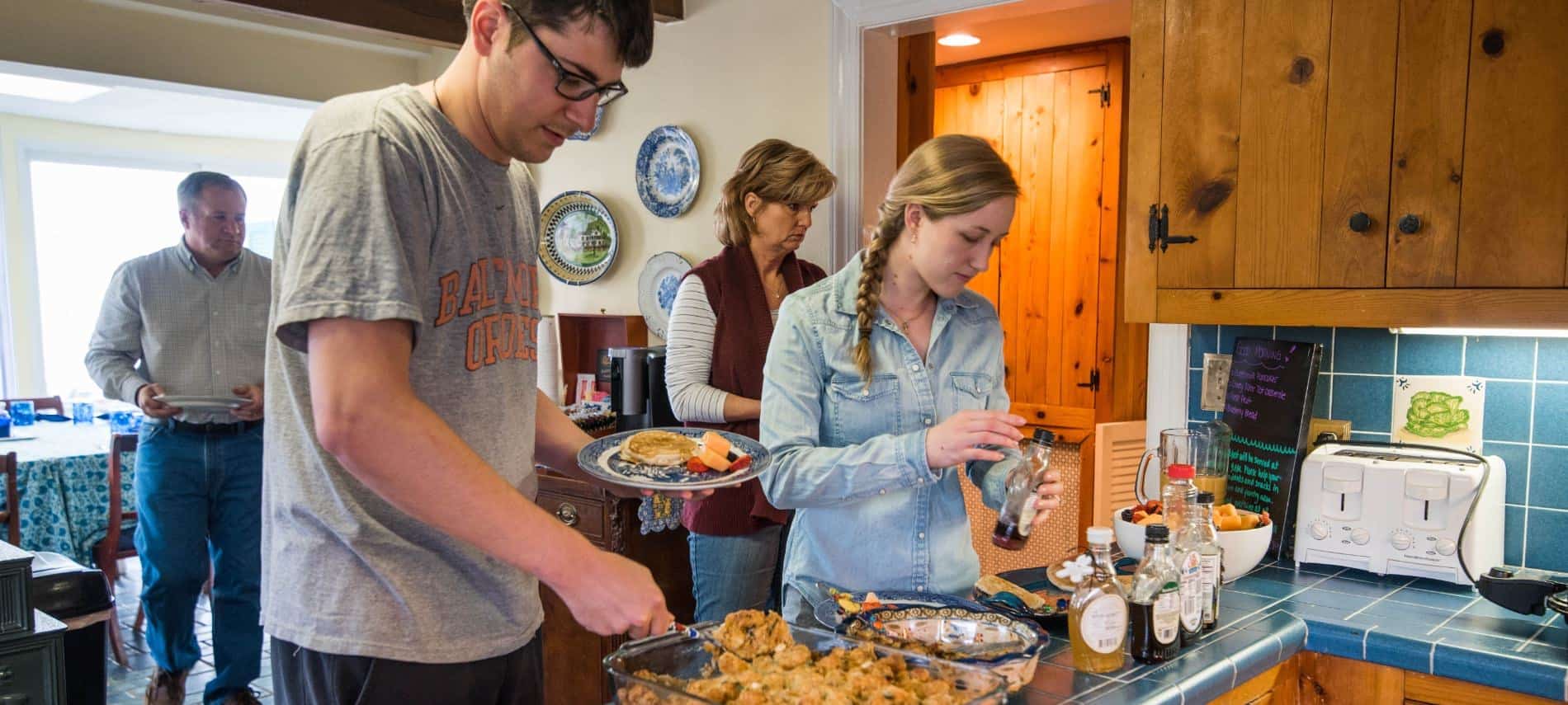 People standing in kitchen serving themselves breakfast