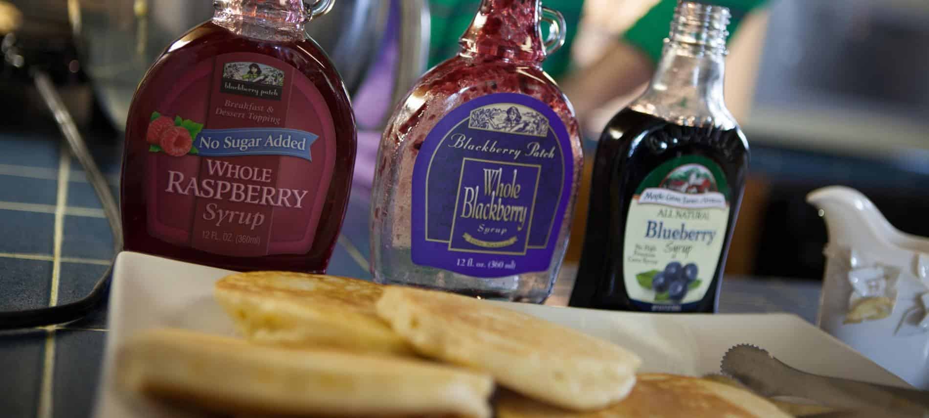 Close up view of pancakes on white platter and three different syrups