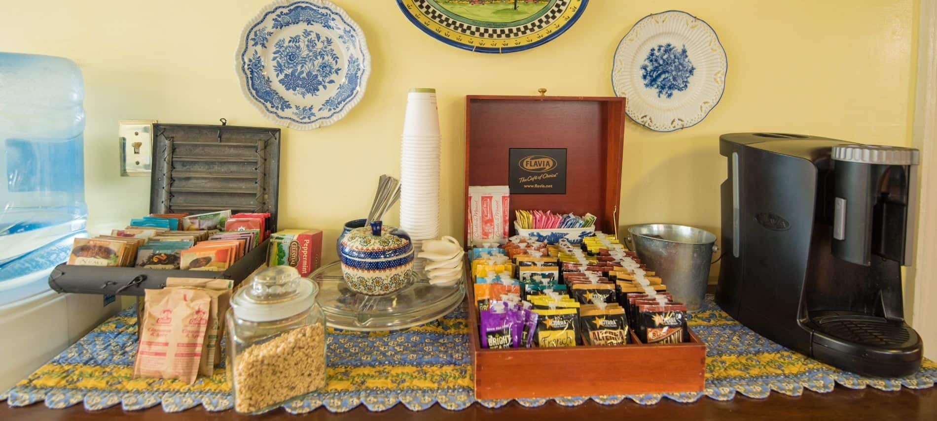 Coffee maker, box with a variety of coffee, box with a variety of teas, and a variety of oatmeal sitting on a wooden table