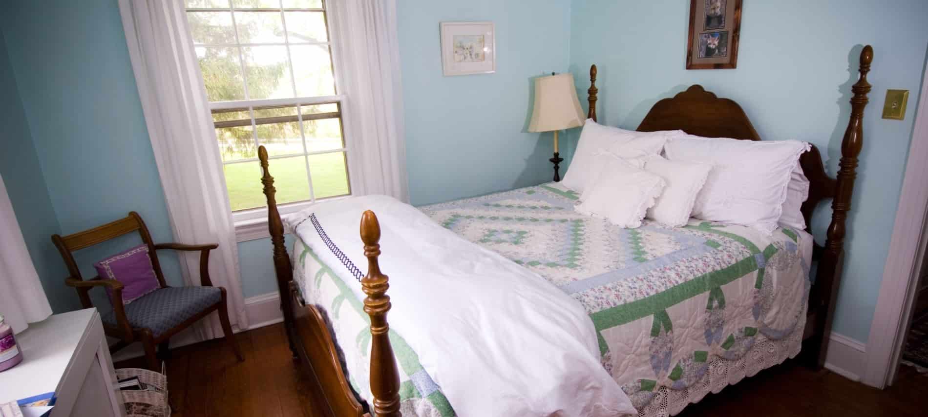 Bedroom with dark wood furntiure, green, light blue and white quilt, and light blue walls