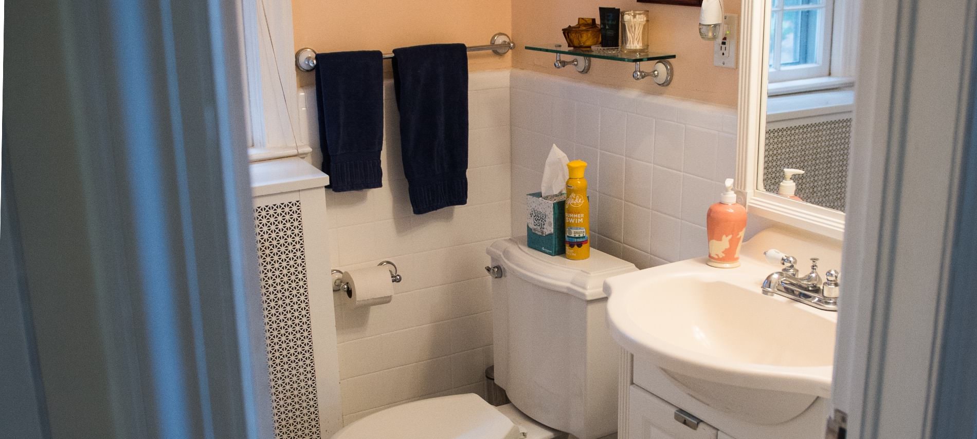 Bathroom with white tiled and peach walls, white sink, white toilet, and navy towels