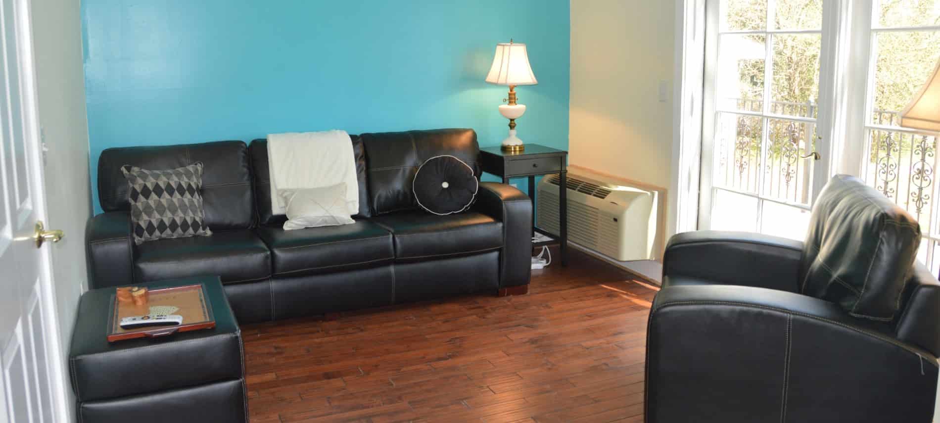 Living room with dark leather couch, chair and ottoman, hardwood floors, and turquoise accent wall