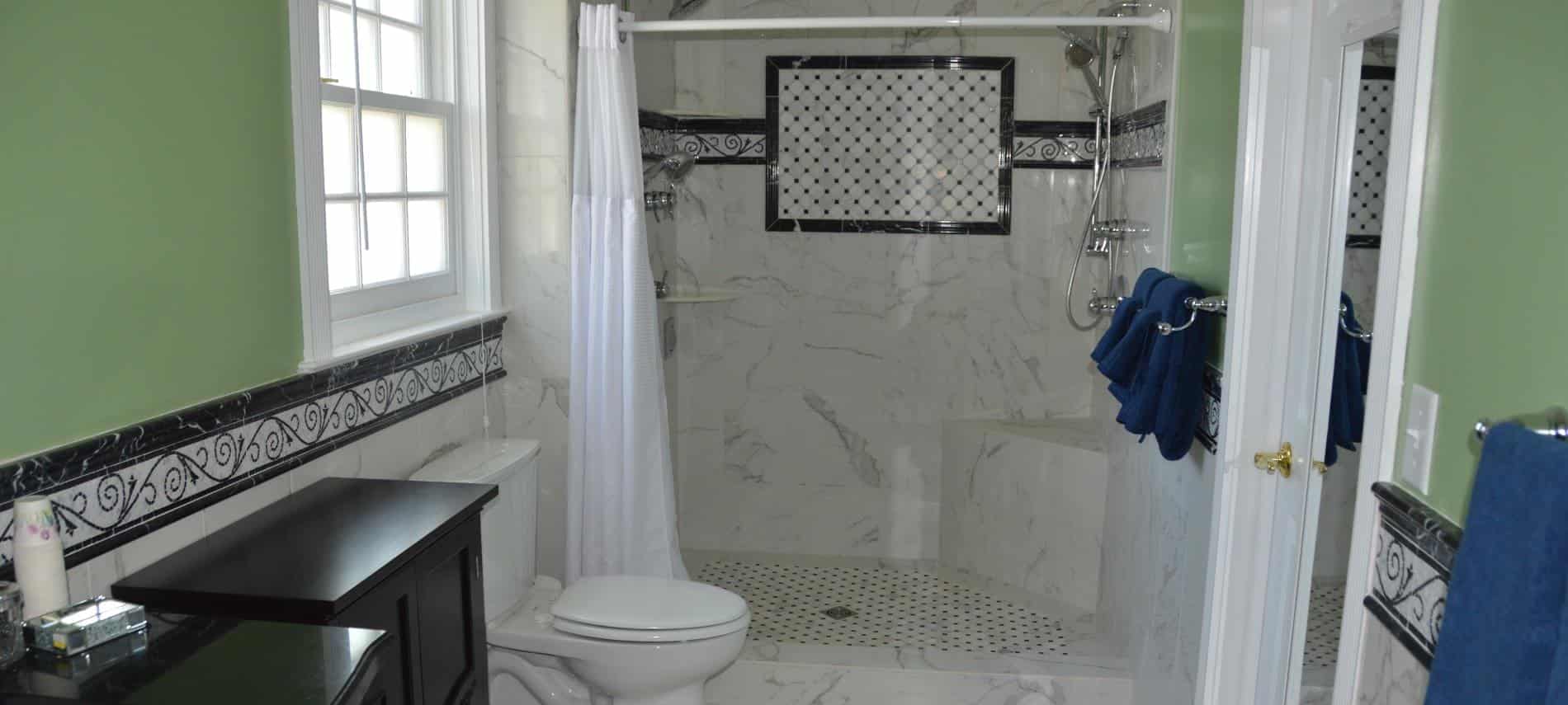 Bathroom with marble tiled floors, wall, and walk in shower with black and white tile accents and white shower curtain