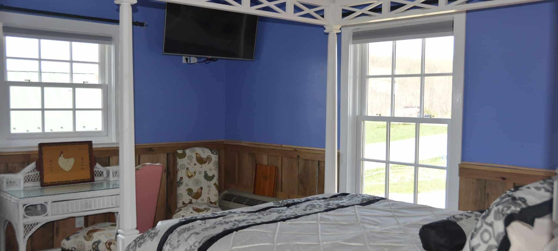 Bedroom with white wooden four-post canopy bed, white and black bedding, wood wainscoating, blue walls, and flat-screen tv mounted on wall
