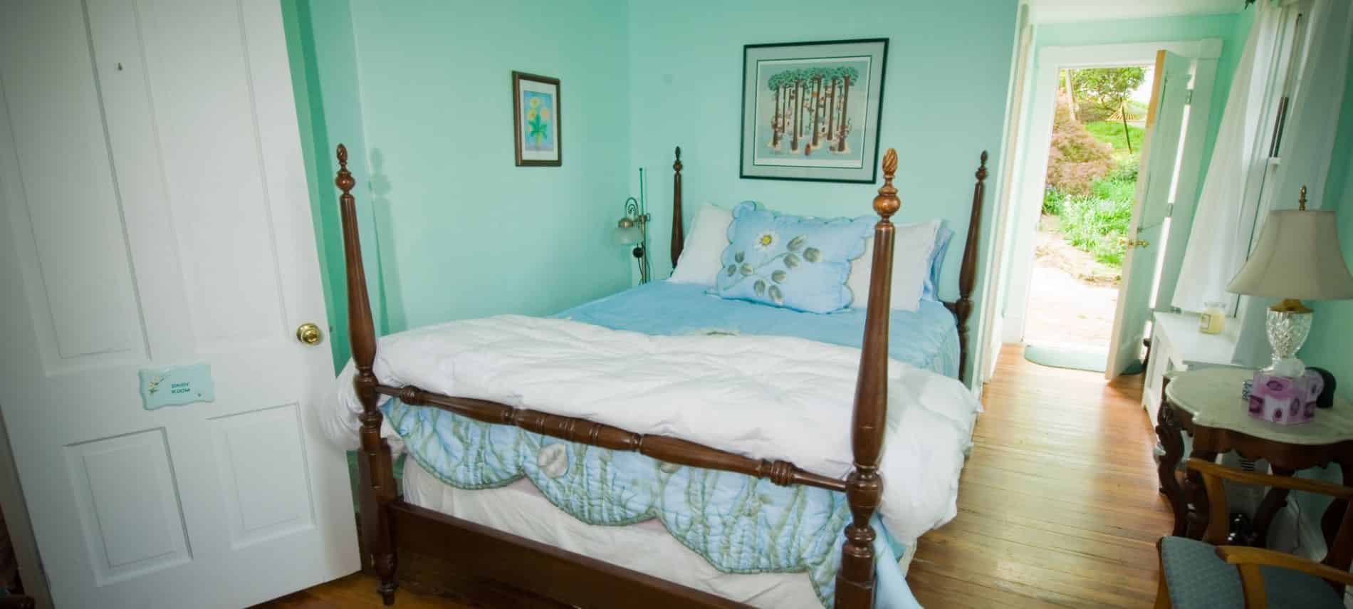 Bedroom with dark wooden furniture and four-post bed, white and blue bedding, hardwood floors, and mint colored walls