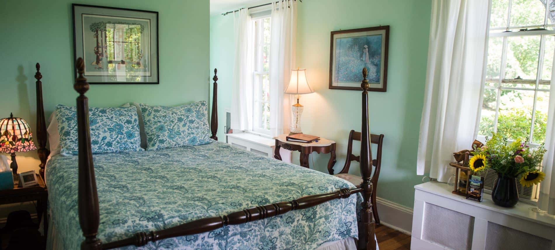 Bedroom with dark wooden furniture and four-post bed, white and blue bedding, hardwood floors, and mint colored walls