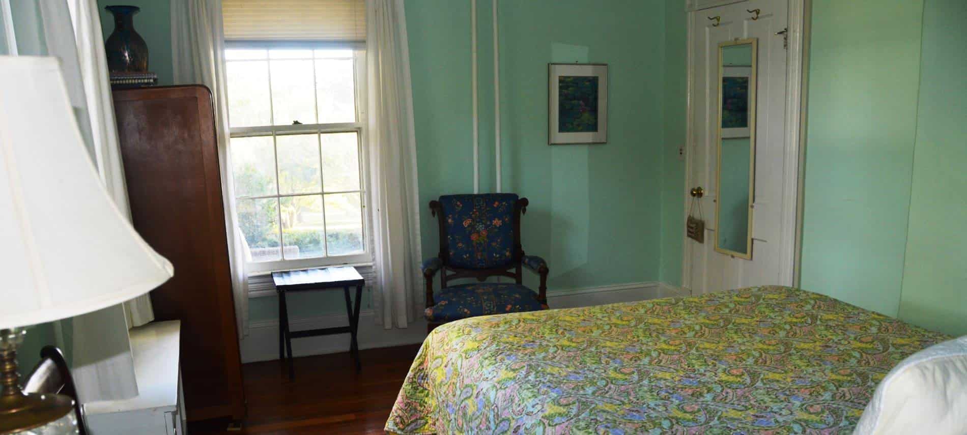 Bedroom with dark wooden furniture, yellow, blue and green floral bedding, hardwood floors, and mint colored walls