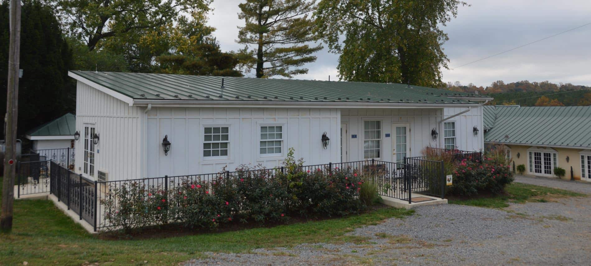 Exterior view of Chicken Coop painted white with green roof surrounded by rod iron fence and rose bushes