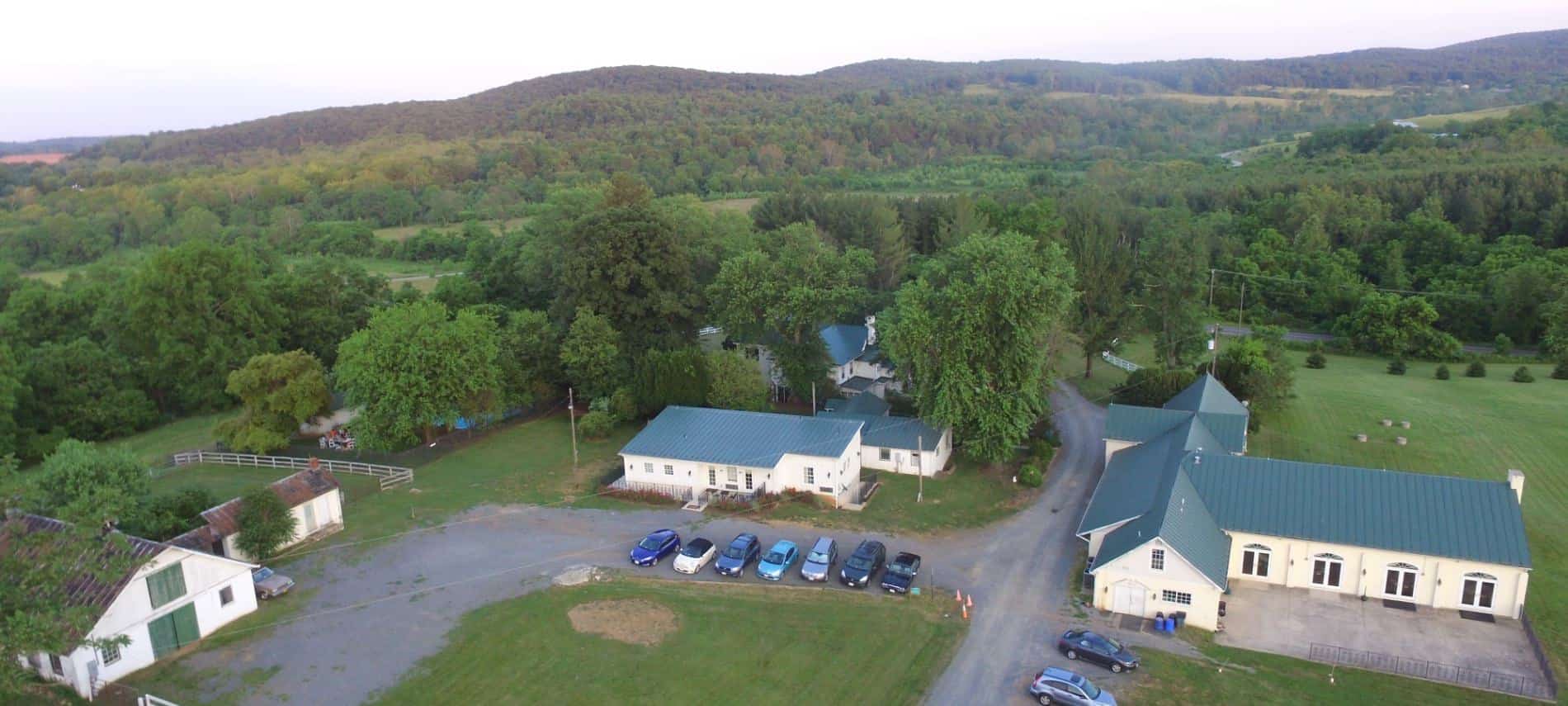 Aerial view of the property surrounded by large trees and green fields