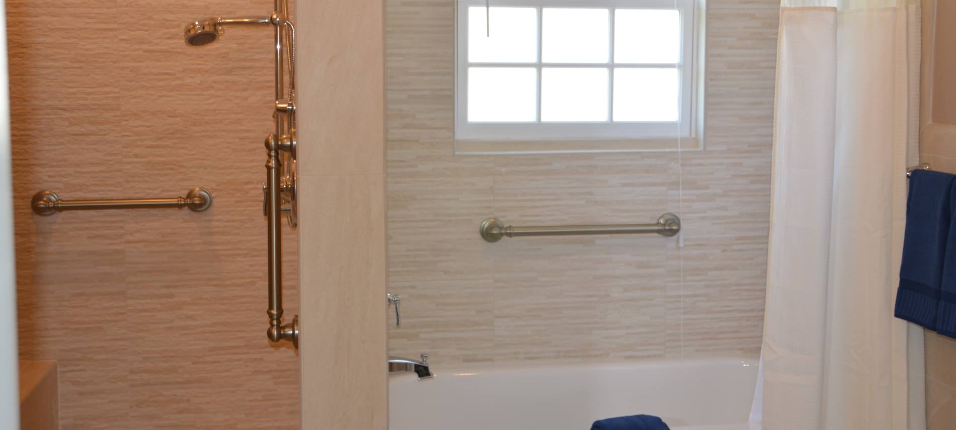 Bathroom with tiled walls in separate shower area and tub area with white curtain and navy towels