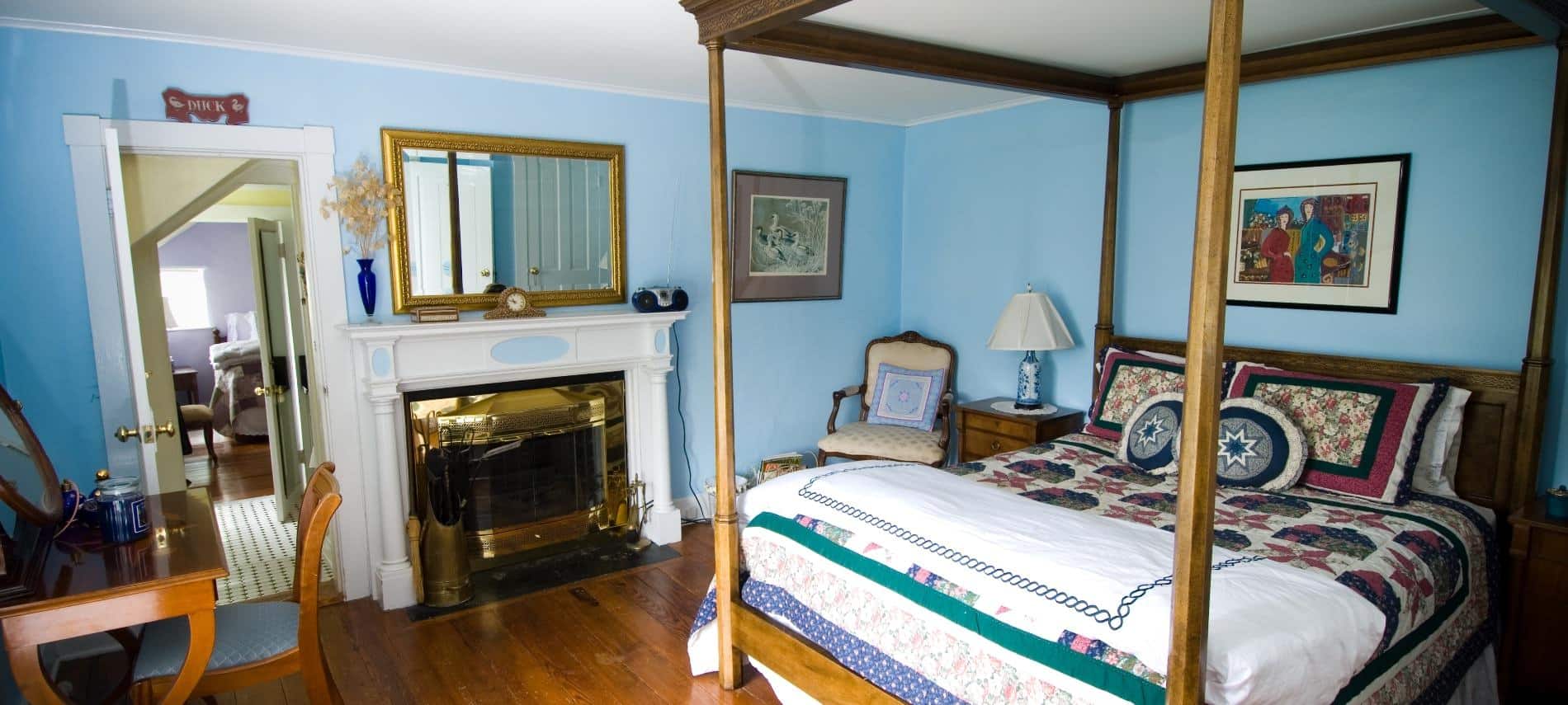 Bedroom with dark wooden furniture and four-post canopy bed, navy, burgundy and white quilt, hardwood floors, fireplace, and blue walls