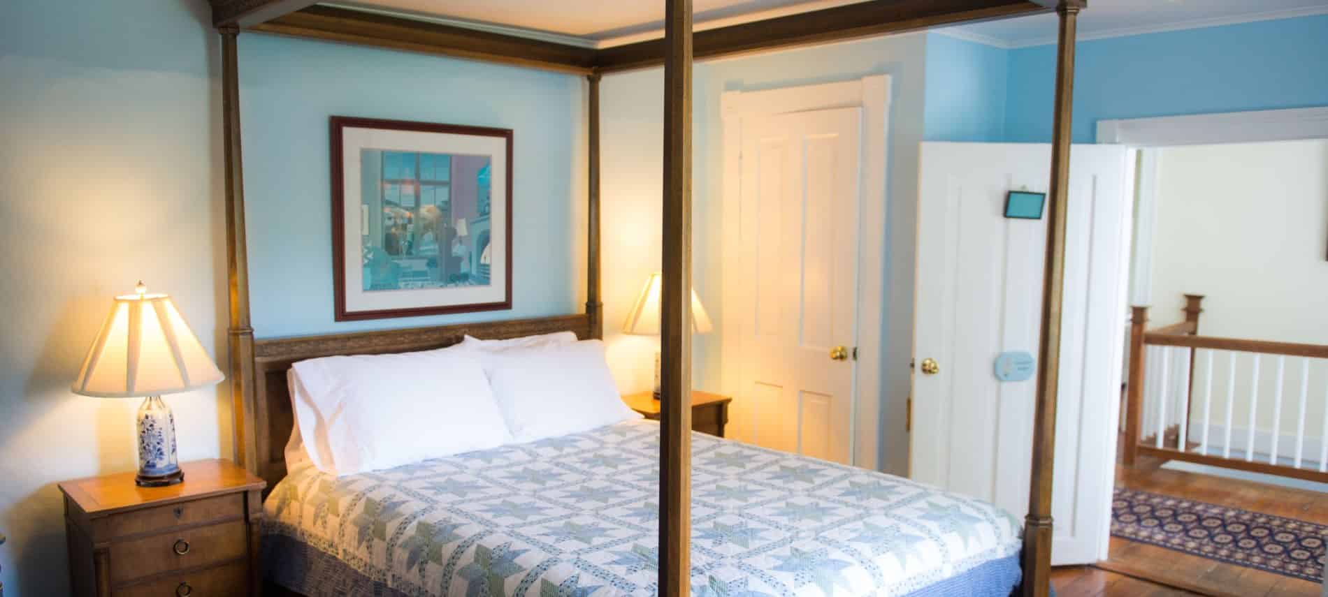 Bedroom with dark wooden furniture and four-post canopy bed, light blue, green and white quilt, hardwood floors, and blue walls