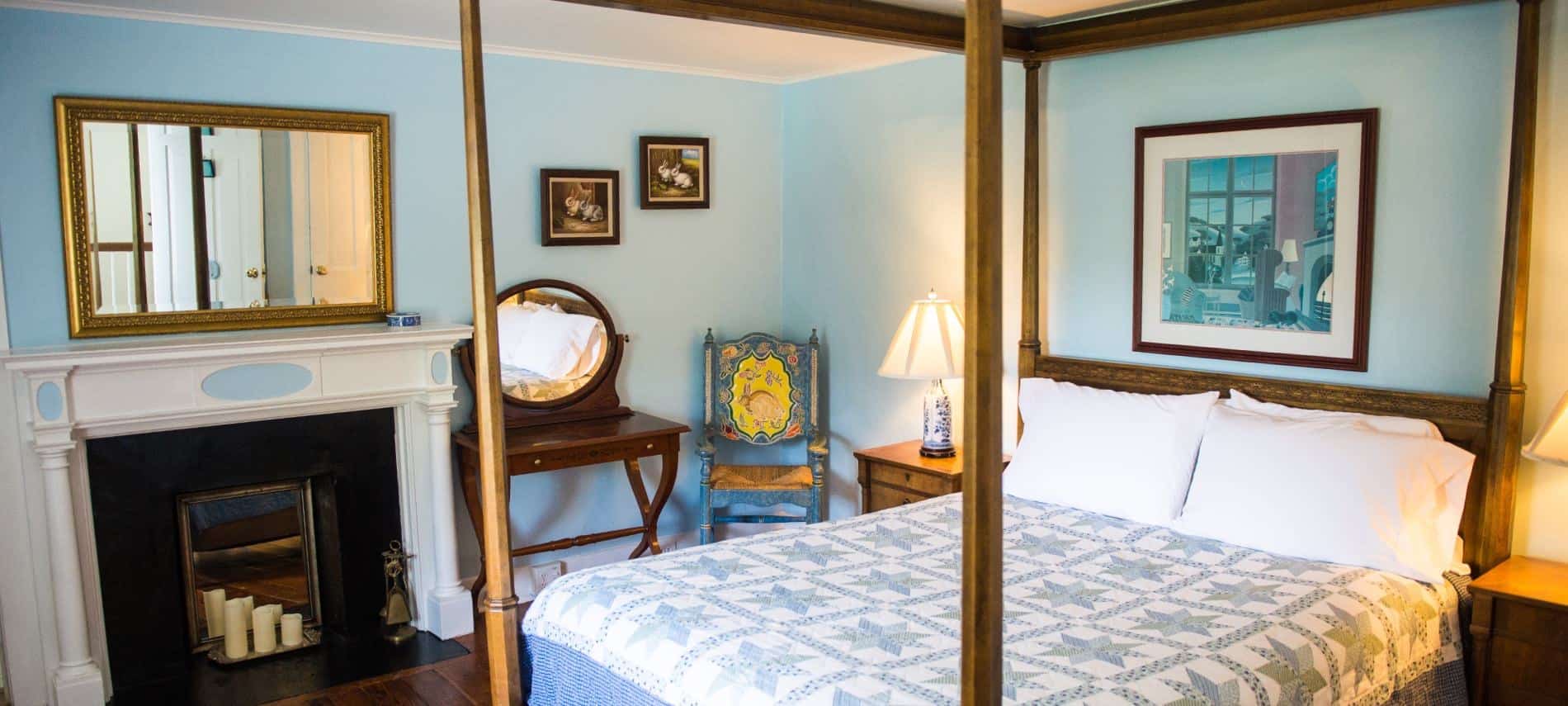 Bedroom with dark wooden furniture and four-post canopy bed, light blue, green and white quilt, fireplace, hardwood floors, and blue walls