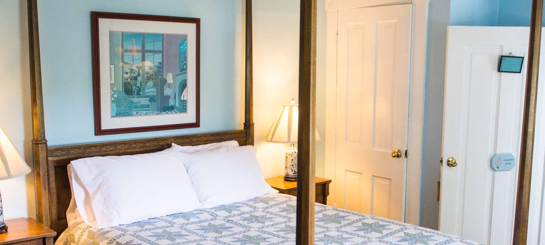 Bedroom with dark wooden furniture and four-post canopy bed, light blue, green and white quilt, hardwood floors, and blue walls