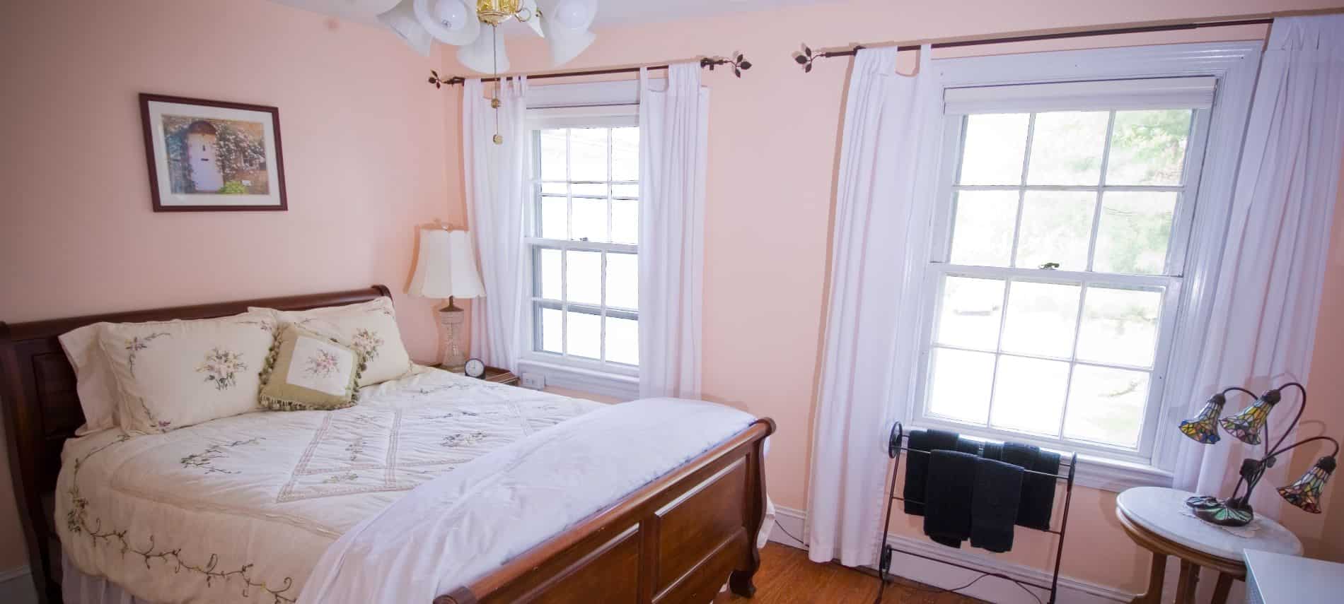 Bedroom with dark wooden sleigh bed, white and cream bedding, hardwood floors, and light pink walls