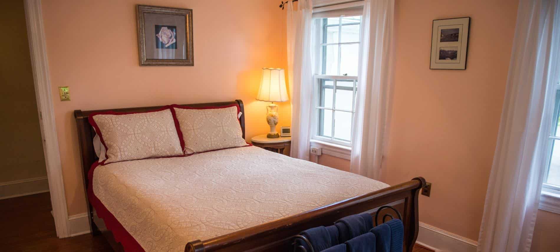 Bedroom with dark wooden sleigh bed, white and cream bedding, hardwood floors, and light pink walls