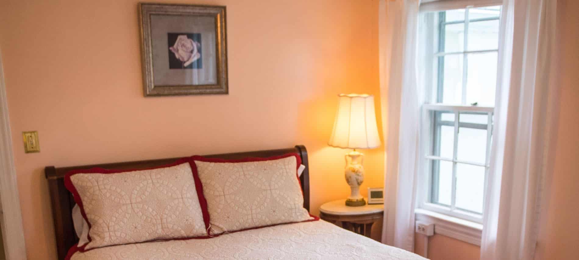 Bedroom with dark wooden sleigh bed, white and cream bedding, and light pink walls