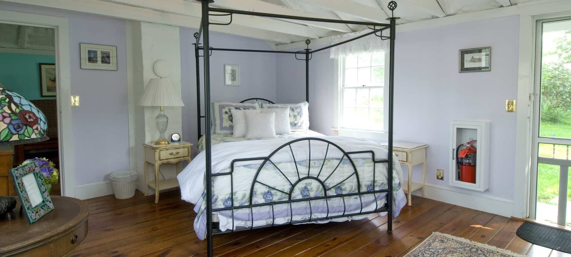 Bedroom with rod iron four-post canopy bed with white and lavender bedding, hardwood flooring, and lavender walls