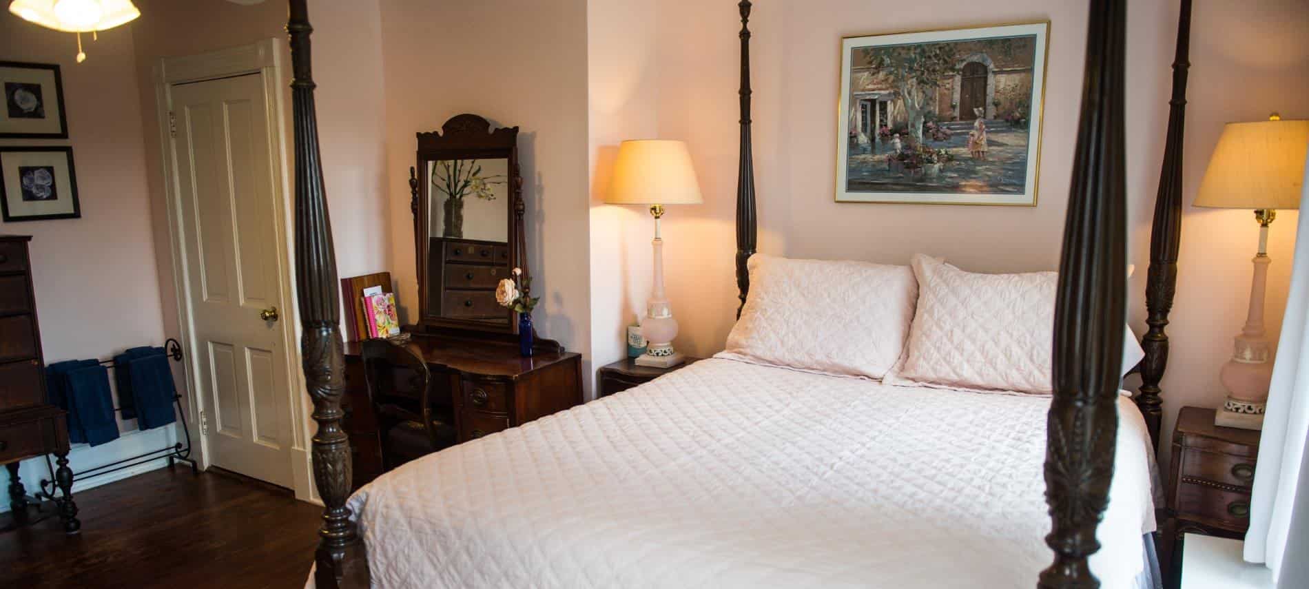 Bedroom with dark wood four-post bed with light pink bedding, hardwood floors, and light pink walls