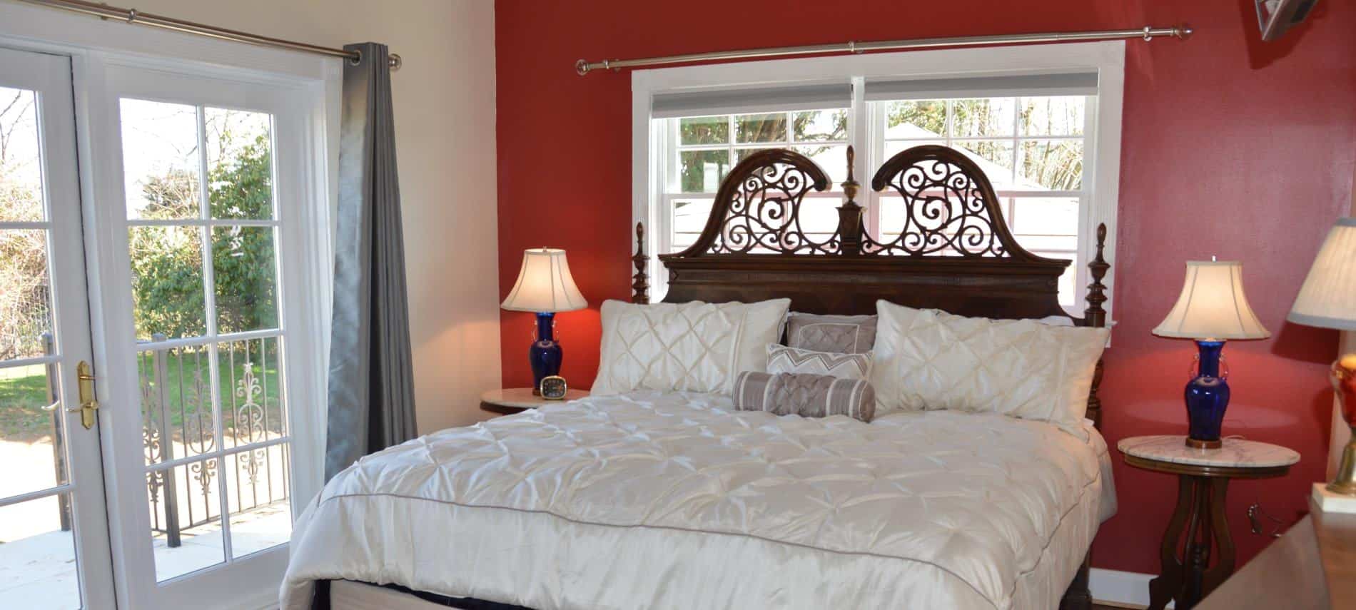 Bedroom with dark wooden ornate headboard, white bedding, hardwood floors, and dark red accent wall